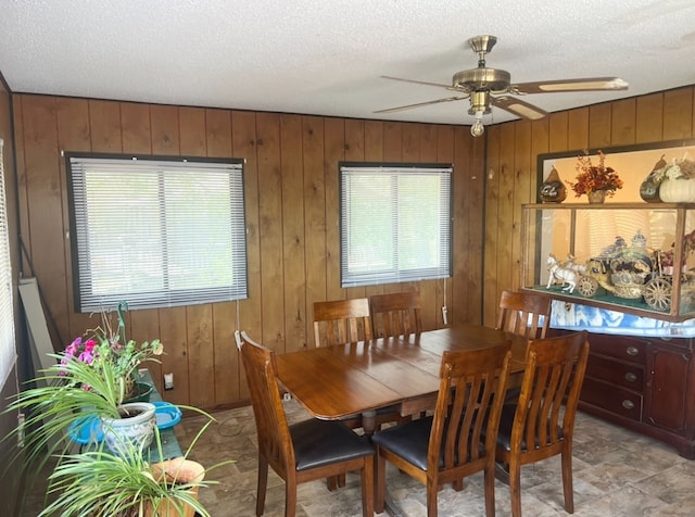 dining area with ceiling fan, wooden walls, a healthy amount of sunlight, and a textured ceiling