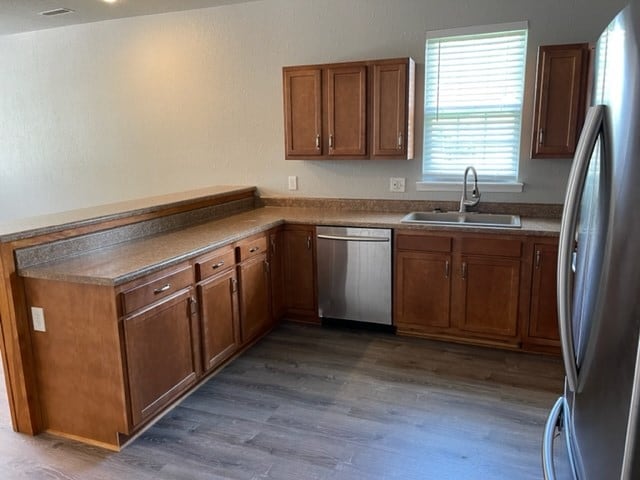 601/603 W Laharpe St, Kirksville, MO 63501 - kitchen with a peninsula, brown cabinets, appliances with stainless steel finishes, a sink, and wood finished floors
