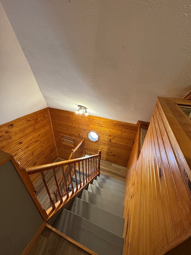 stairway with hardwood / wood-style floors, a textured ceiling, and wooden walls