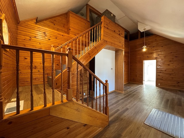 stairs featuring high vaulted ceiling, wooden walls, and wood-type flooring