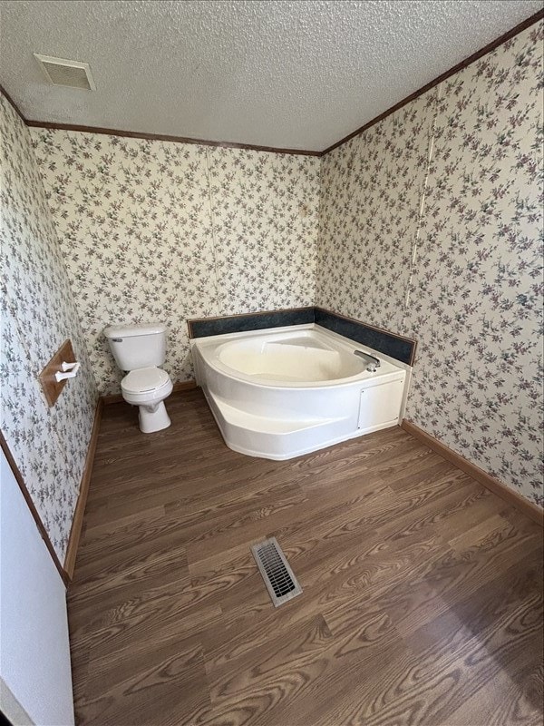 bathroom with hardwood / wood-style floors, a bathtub, toilet, ornamental molding, and a textured ceiling