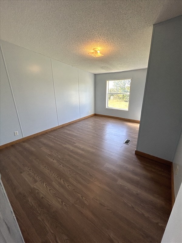 empty room with a textured ceiling and dark hardwood / wood-style floors