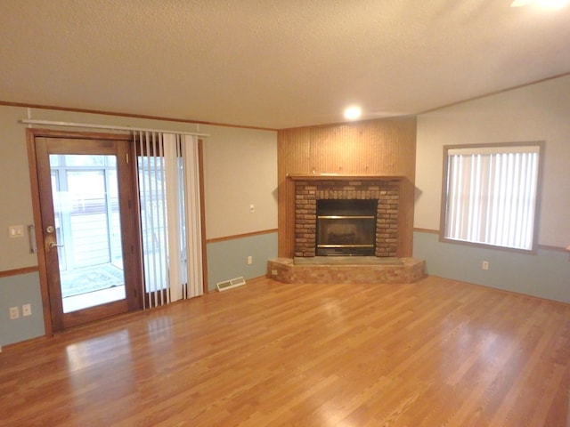 unfurnished living room featuring a textured ceiling, a fireplace, visible vents, and wood finished floors