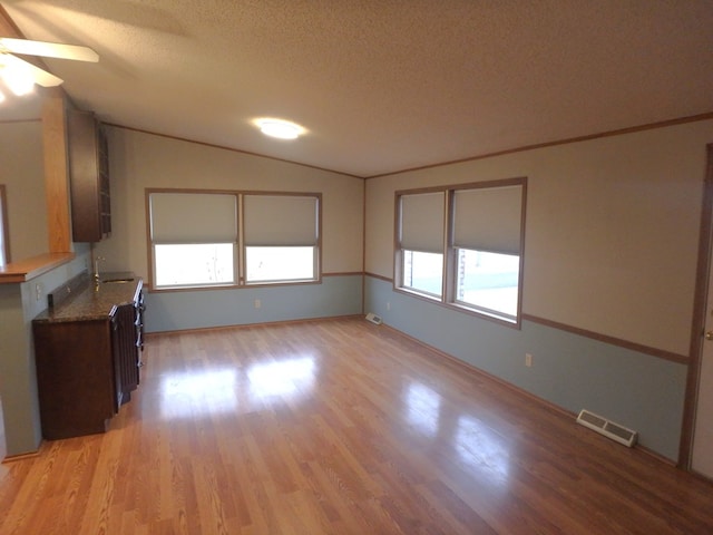 interior space featuring visible vents, ceiling fan, vaulted ceiling, a textured ceiling, and light wood-style floors