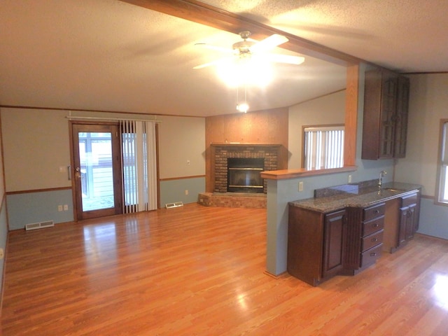 kitchen with a peninsula, light wood-style flooring, a fireplace, and visible vents