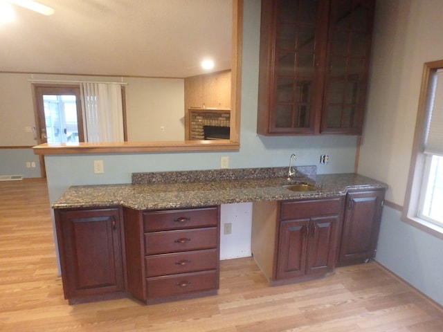 kitchen with dark stone counters, light wood finished floors, a sink, and glass insert cabinets