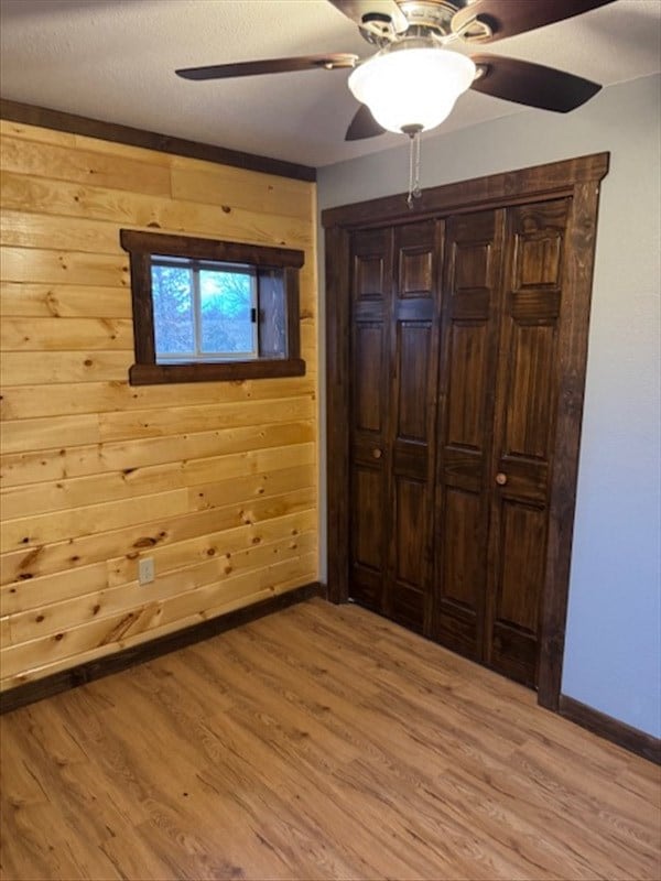 unfurnished bedroom featuring a textured ceiling, light wood-type flooring, ceiling fan, and wooden walls