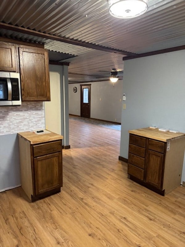 kitchen featuring wooden counters, decorative backsplash, dark brown cabinets, ceiling fan, and light hardwood / wood-style flooring