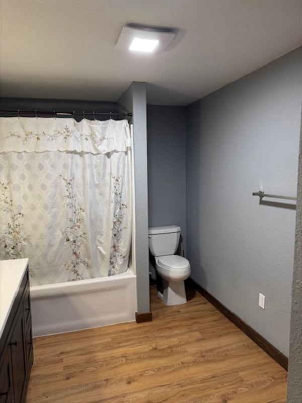 full bathroom with hardwood / wood-style floors, vanity, shower / bath combination with curtain, and toilet