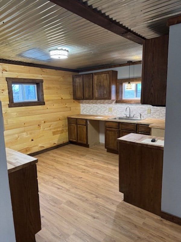 kitchen featuring wood walls, sink, hanging light fixtures, light hardwood / wood-style floors, and dark brown cabinetry