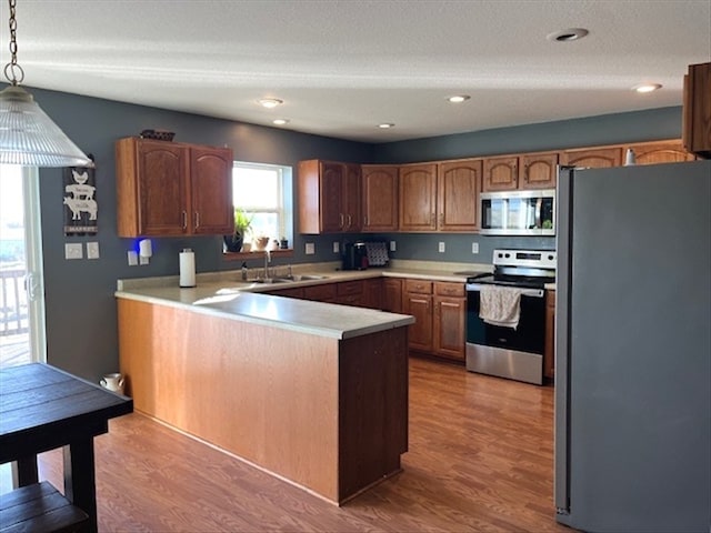 kitchen featuring sink, hanging light fixtures, light hardwood / wood-style flooring, kitchen peninsula, and appliances with stainless steel finishes