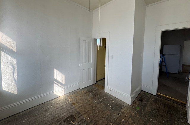 empty room with a towering ceiling, crown molding, baseboards, and hardwood / wood-style flooring