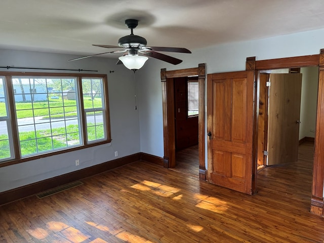 spare room with baseboards, ceiling fan, dark wood finished floors, and visible vents