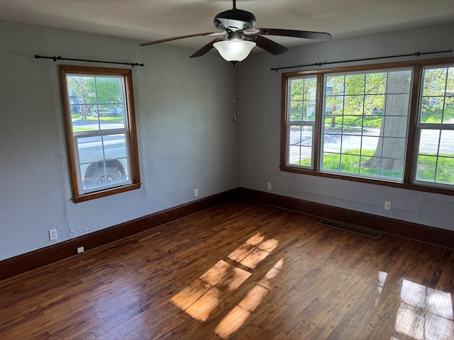 unfurnished room with baseboards, a ceiling fan, dark wood-type flooring, and visible vents