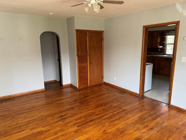 spare room featuring arched walkways, ceiling fan, baseboards, and wood finished floors