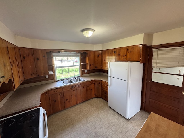 kitchen featuring brown cabinets, electric range, a sink, freestanding refrigerator, and light floors