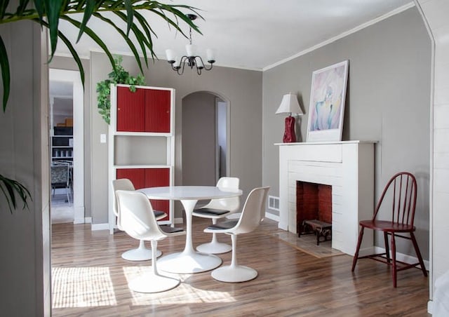 dining area featuring wood-type flooring, an inviting chandelier, a brick fireplace, and crown molding