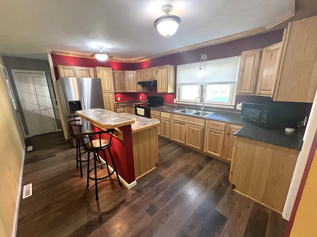 kitchen featuring a sink, black appliances, a breakfast bar, under cabinet range hood, and dark wood-style flooring