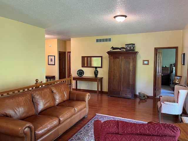 living room featuring a textured ceiling, visible vents, wood finished floors, and baseboards
