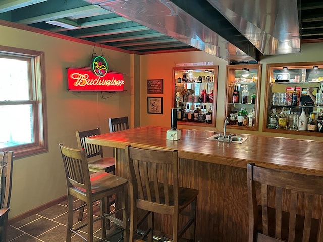 bar with a wealth of natural light, dark tile patterned flooring, a sink, and indoor wet bar