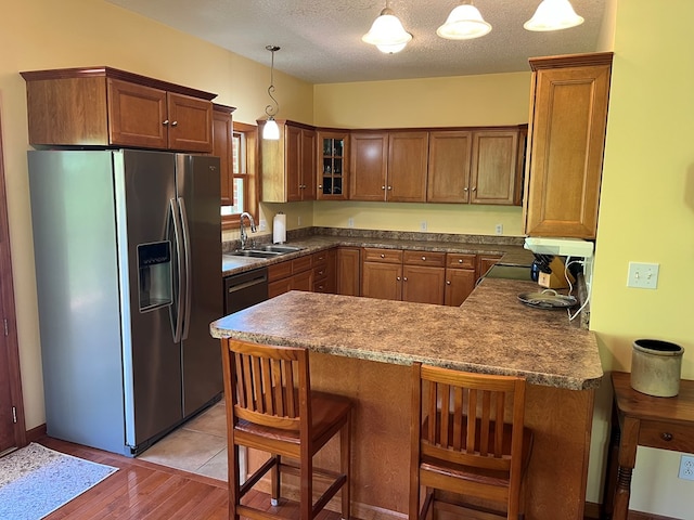 kitchen with a sink, a peninsula, brown cabinetry, stainless steel fridge, and glass insert cabinets