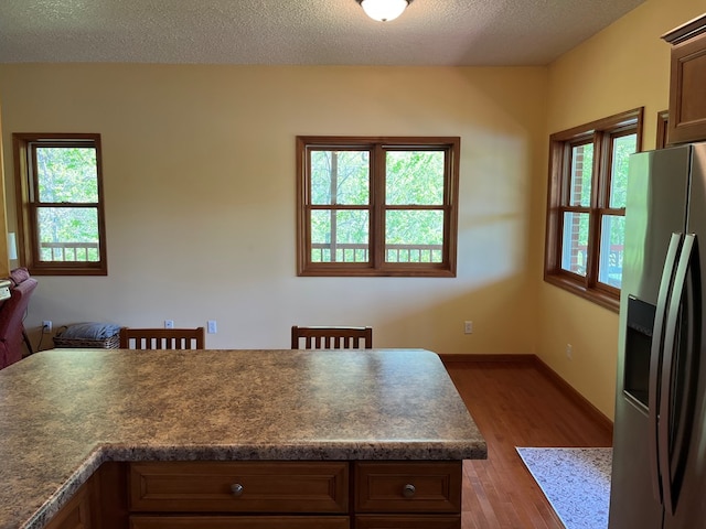 kitchen featuring a textured ceiling, stainless steel fridge, dark countertops, and wood finished floors