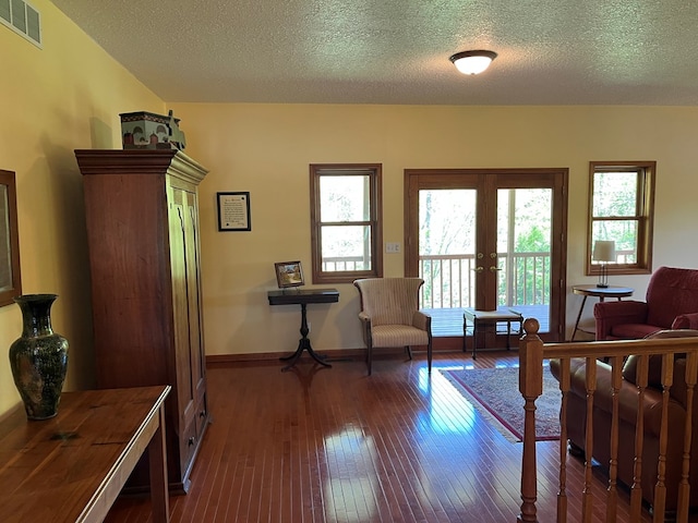 living area with a healthy amount of sunlight, dark wood-style flooring, french doors, and visible vents