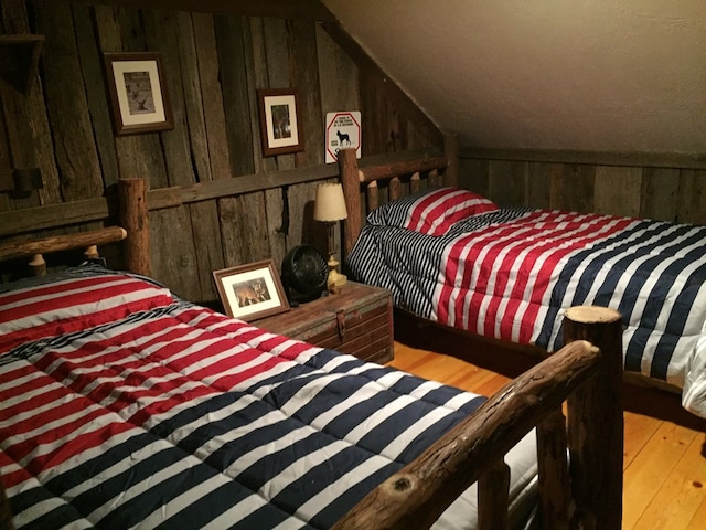 bedroom featuring wood walls, light hardwood / wood-style floors, and vaulted ceiling