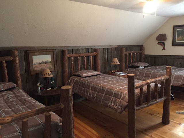 bedroom with hardwood / wood-style flooring, lofted ceiling, and wooden walls