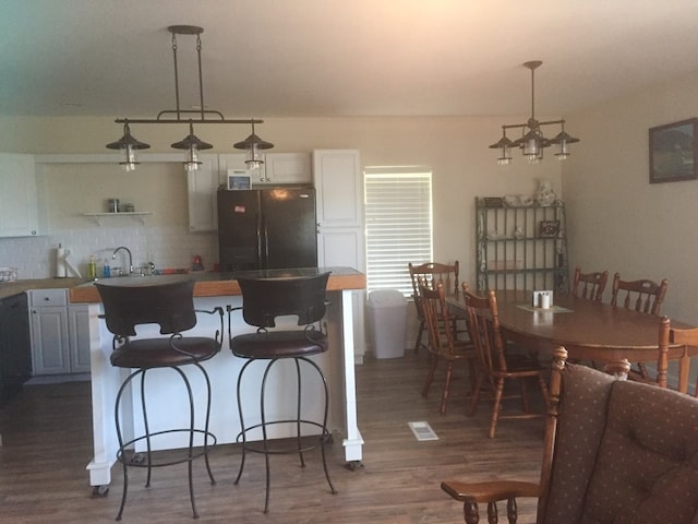 kitchen featuring black refrigerator, decorative backsplash, decorative light fixtures, dark hardwood / wood-style floors, and white cabinetry