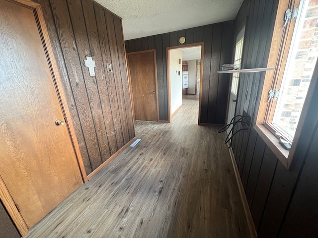 corridor featuring wooden walls, a textured ceiling, and wood finished floors