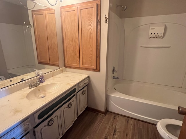 full bath featuring baseboards, toilet, wood finished floors, vanity, and washtub / shower combination