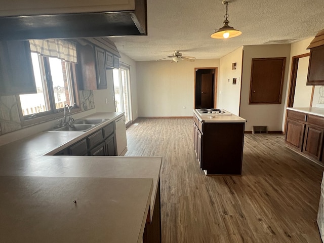 kitchen with light countertops, a kitchen island, a sink, a textured ceiling, and wood finished floors