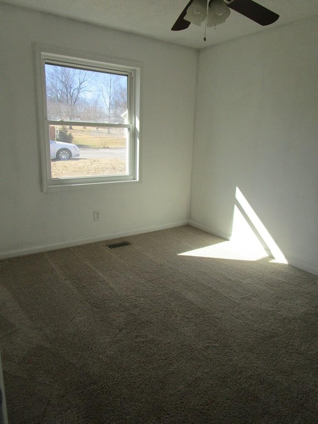 carpeted empty room featuring ceiling fan, visible vents, and baseboards