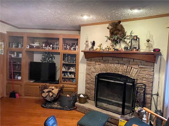 living area featuring ornamental molding, a stone fireplace, a textured ceiling, and wood finished floors