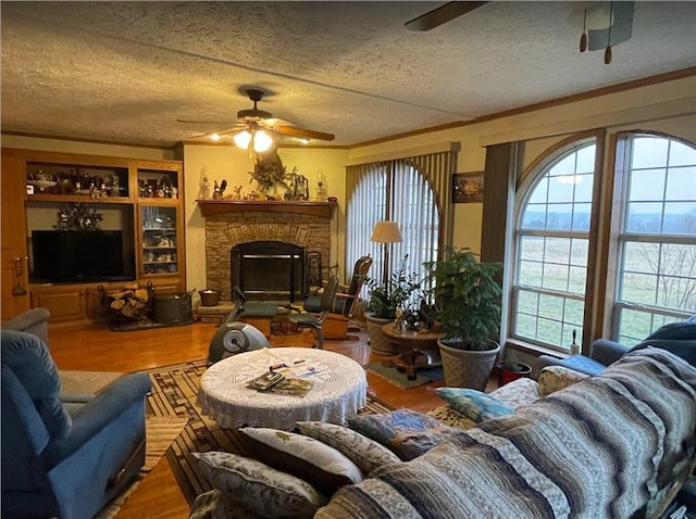 living area with a textured ceiling, a stone fireplace, wood finished floors, and a ceiling fan