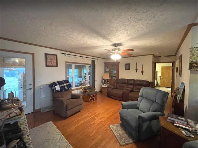 living room featuring a textured ceiling, light wood finished floors, ornamental molding, and a ceiling fan