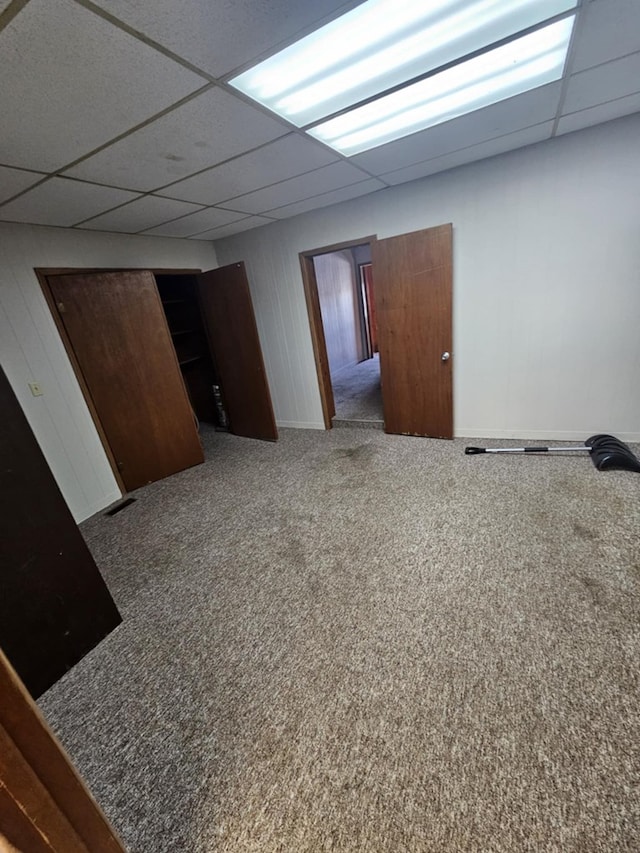 carpeted empty room featuring baseboards and a drop ceiling