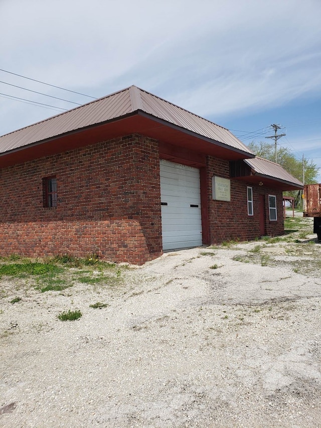 view of property exterior featuring an attached garage, metal roof, and brick siding