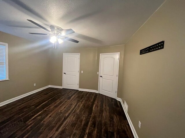 empty room featuring ceiling fan, dark wood-type flooring, and a textured ceiling