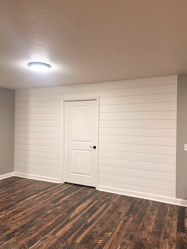 unfurnished room featuring wood walls, dark hardwood / wood-style floors, and a textured ceiling