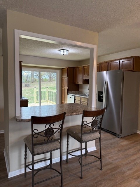 kitchen featuring a textured ceiling, a kitchen bar, stainless steel fridge with ice dispenser, and dark wood-type flooring