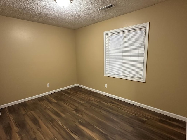 empty room featuring visible vents, dark wood finished floors, a textured ceiling, and baseboards