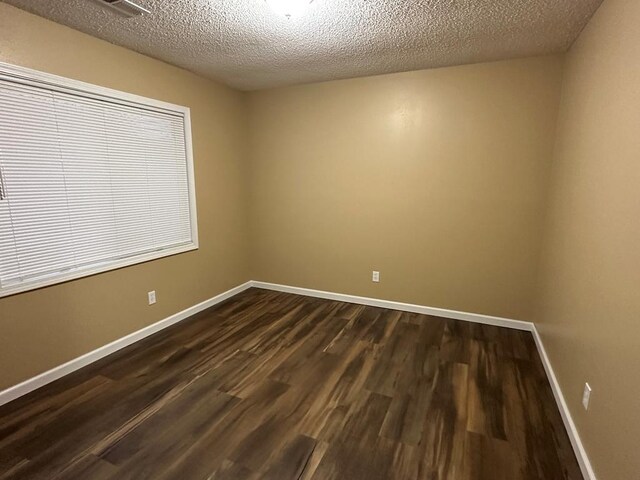 spare room featuring baseboards, dark wood finished floors, and a textured ceiling