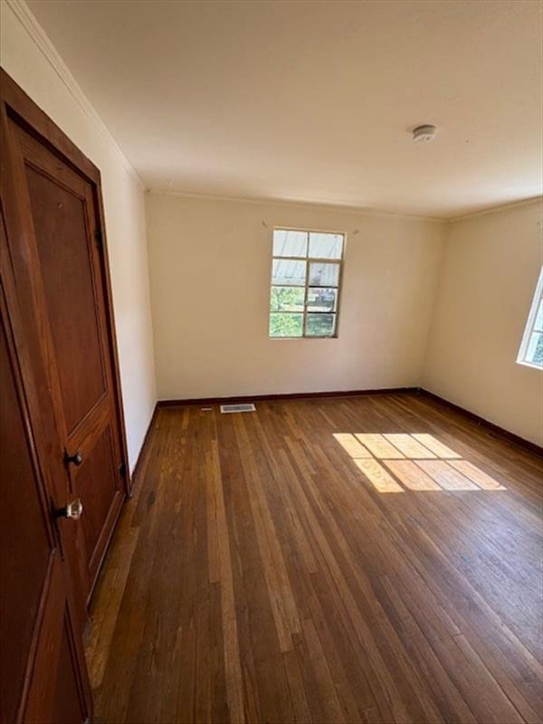 unfurnished room with ornamental molding and dark wood-type flooring