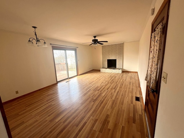 unfurnished living room featuring a brick fireplace, ceiling fan with notable chandelier, and wood-type flooring