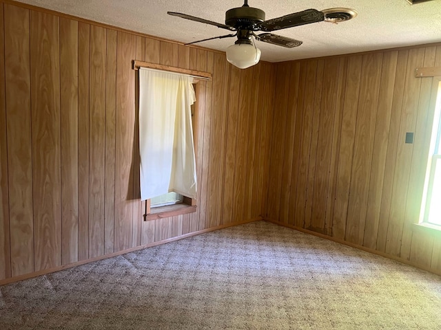 empty room featuring ceiling fan, wooden walls, carpet, and a textured ceiling