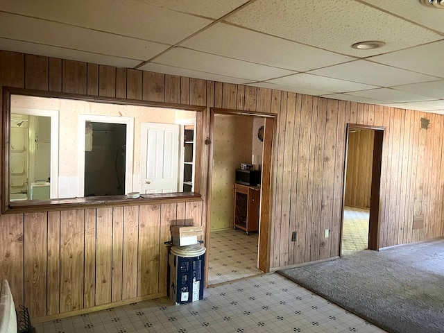 spare room with a paneled ceiling, wood walls, light carpet, and washer / clothes dryer