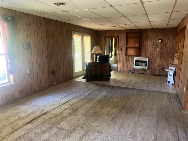 unfurnished room with carpet floors, heating unit, a drop ceiling, and wood walls