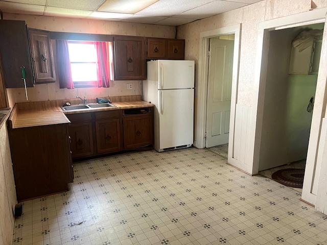 kitchen with dark brown cabinetry, sink, white fridge, and a drop ceiling